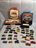 Full lineup of mostly Matchbox and Hot Wheels cars arranged on a couch with two carrying cases behind them and the remote control tractor playset in packaging.