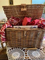 Front view of the open wicker picnic basket showing the woven texture and leather strap, with red patterned and solid red napkins inside.