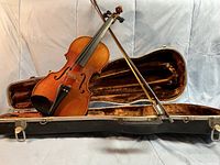 Violin placed partially inside the open case along with the bow shown behind it.
