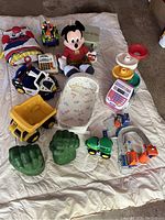 Full view of all toddler toys arranged on a blanket showing multiple toys including Mickey Mouse plush, toy vehicles, cash register, and activity toys.