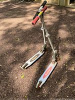 Two foldable Razor kick scooters side by side on ground, visible pink and black handle grips, silver frames