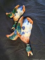 Two vintage porcelain duck figurines lying on black cloth, showing painted details and markings.