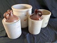 Four vintage crocks including two jugs, displayed against black fabric backdrop