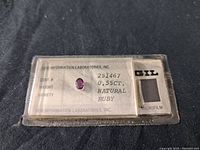 Close-up photo of natural ruby gemstone in certification holder showing stone and lab details.