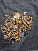 Photo showing a large pile of assorted vintage and antique pins in various styles and materials piled together on a dark fabric background.