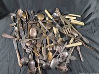 Top view of assorted vintage silverware including forks, spoons with various handles in a pile showing tarnish and wear.