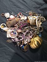 Overhead image showing a pile of assorted vintage costume jewelry including necklaces, earrings, brooches, and watches in used condition.