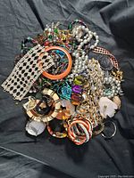 Top-down view of assorted vintage costume jewelry mixed pile. Includes necklaces, bracelets, earrings made of beads, metals, faux pearls, and enamel in various colors and styles.