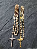 Photo of two cross necklaces laid flat on a dark fabric background, showing entire length of beaded chains and crucifix pendants.