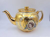 Photo of the sided view of the gold gild teapot showing the portrait, lion emblem, handle, and spout.