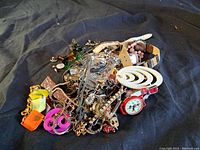 Pile of various vintage jewelry and watches, showing mixed earrings, chains, a red watch, and other accessories in a heap.