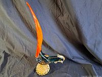 Front/side view of the large glass rooster sculpture showing the clear amber textured base, dark body with bubbles, and tall red tail.