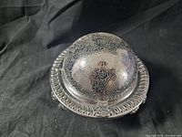 Full view of silver butter dish with domed lid closed showing intricate floral engravings and ornate rim.