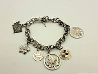 Full view of sterling silver chain bracelet with six attached charms: state map, flower, bird, maple leaf, dice, and fishing lure.