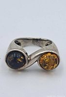Front view of the sterling silver ring showing two different colored round amber stones set side-by-side in bezel setting.