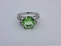 Front view showing round green faceted gemstone set in silver with detailed band and side accents.