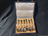 Opened blue case showing six sterling silver spoons each with jade stones inlaid in the handles.