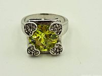 Close-up front view of the sterling silver ring with square-cut green peridot and heart-shaped prongs accented by small clear stones.