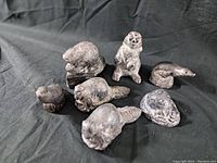 Lot of seven vintage stone animal figures including rabbit, beaver, snake, otter, and others on dark fabric background.