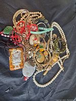 Mixed pile of various costume jewelry items showing necklaces, pendants, bracelets and watches on black cloth background.