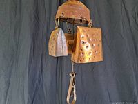 Front angled view of vintage copper bell showing domed top, two attached hammered plates (one square, one rectangular), hanging loop, and pull handle.