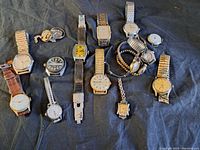 Photo of 15 vintage watches laid out on dark fabric surface showing various watch types and bands.