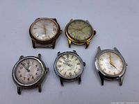 Five vintage watch heads arranged on white surface.