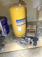 Yellow 7 gallon portable upright air tank with label showing brand and capacity, placed on workbench with pneumatic tools and fittings nearby.