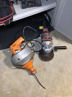 View showing both the orange and metallic electric drain snake and the heavy duty grinder with grinding disc and two handles.