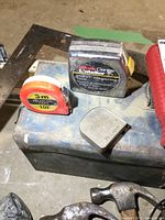 Metal toolbox with various hand tools on top including tape measures and metal square.