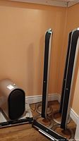 Photo showing two tall LG tower speakers, LG subwoofer, DVD player, and remote control on wooden floor against a beige wall.