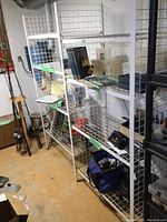 White metal wire shelving unit placed in basement with adjustable shelves. Various items stored temporarily on shelves, including books, plastic containers, tool bags, and other miscellaneous boxes. Visible surface rust on metal.