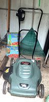 Full view of green Black & Decker lawn mower in storage, shows black handle and overall shape and size.