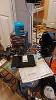 Sony PlayStation 2 console setup with controller, headphones, game discs, instruction manual, and boxed Amazon Echo Dot on a glass table.