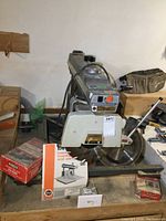 Radial arm saw showing saw blade, motor, and included instruction manual and spare blade boxes arranged on the table.
