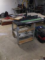 Full view of router table stand with Craftsman router mounted underneath and wood vise on side, showing scale and context in workshop setting.