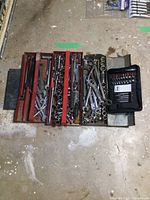 Full view of 3 metal trays filled with assorted wrenches, sockets, ratchets. Black zippered case with socket bits shown on right.