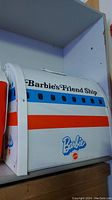 Side view of the Barbie Friendship Ship playset with visible windows, red and blue stripes and handle on top.