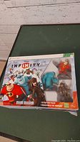Front view of the Disney Infinity 1 Starter Pack for Xbox 360 featuring the game box and visible character figures.