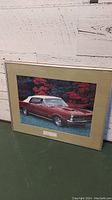 Framed color photograph of a red Pontiac GTO car with white convertible top, displayed against trees in the background. Beige matte and simple frame around the picture.