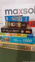 Stack of 6 puzzle boxes showing various puzzle themes and piece counts including Ravensburger and Masterworks