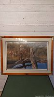 Front view of framed print showing wilderness trapping scene with reflection on glass.