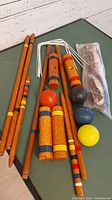 Overall view of vintage croquet set assembled showing wooden mallets, croquet balls in multiple colors, metal wickets, and wooden stakes in bag.