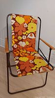 Front view of a vintage lounge chair with brown metal frame, wooden armrests, and colorful floral fabric seat and backrest.