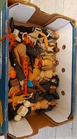 Box filled with multiple vintage plastic action figures, many disassembled or damaged, showing a variety of skin tones and some clothes.