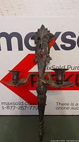 Front view of one metal wall candelabra with detailed leaf and floral design and two candle holders.