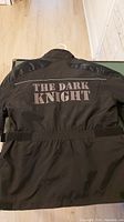 Photo showing back of black Quiksilver men's jacket with large The Dark Knight text across back, size large.