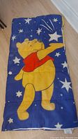 Sleeping bag laid flat showing blue background with white stars and Winnie the Pooh pointing at a shooting star wearing a red shirt.