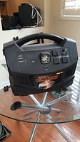 Front view of the black PowerBox showing the Dominator logo, handle, power outlets, switches and LED indicator lights on the control panel.