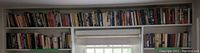Two shelves of assorted fiction and history books, showing many titles in a room with a window underneath the shelves.